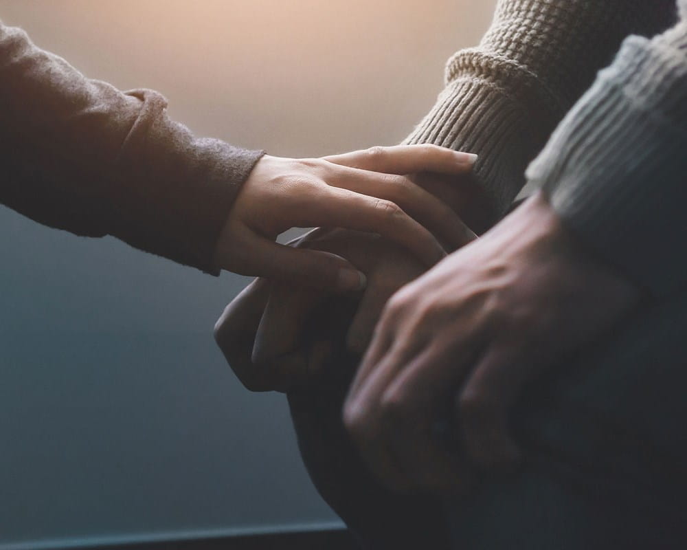 Close up of one friend comforting another showing arms and hands only.