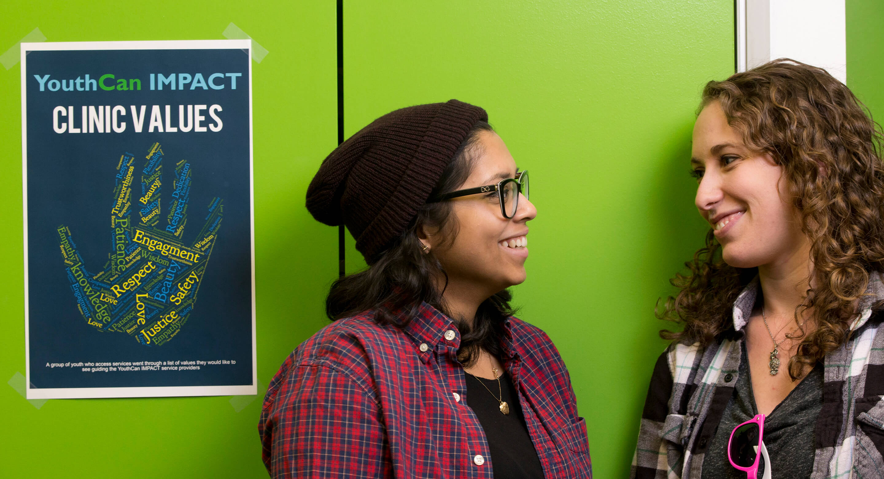 Two female teens beside a YouthCan IMPACT poster