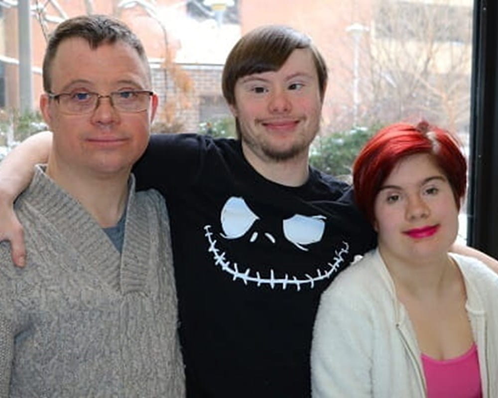 Two men and a woman with Down Syndrome smiling.