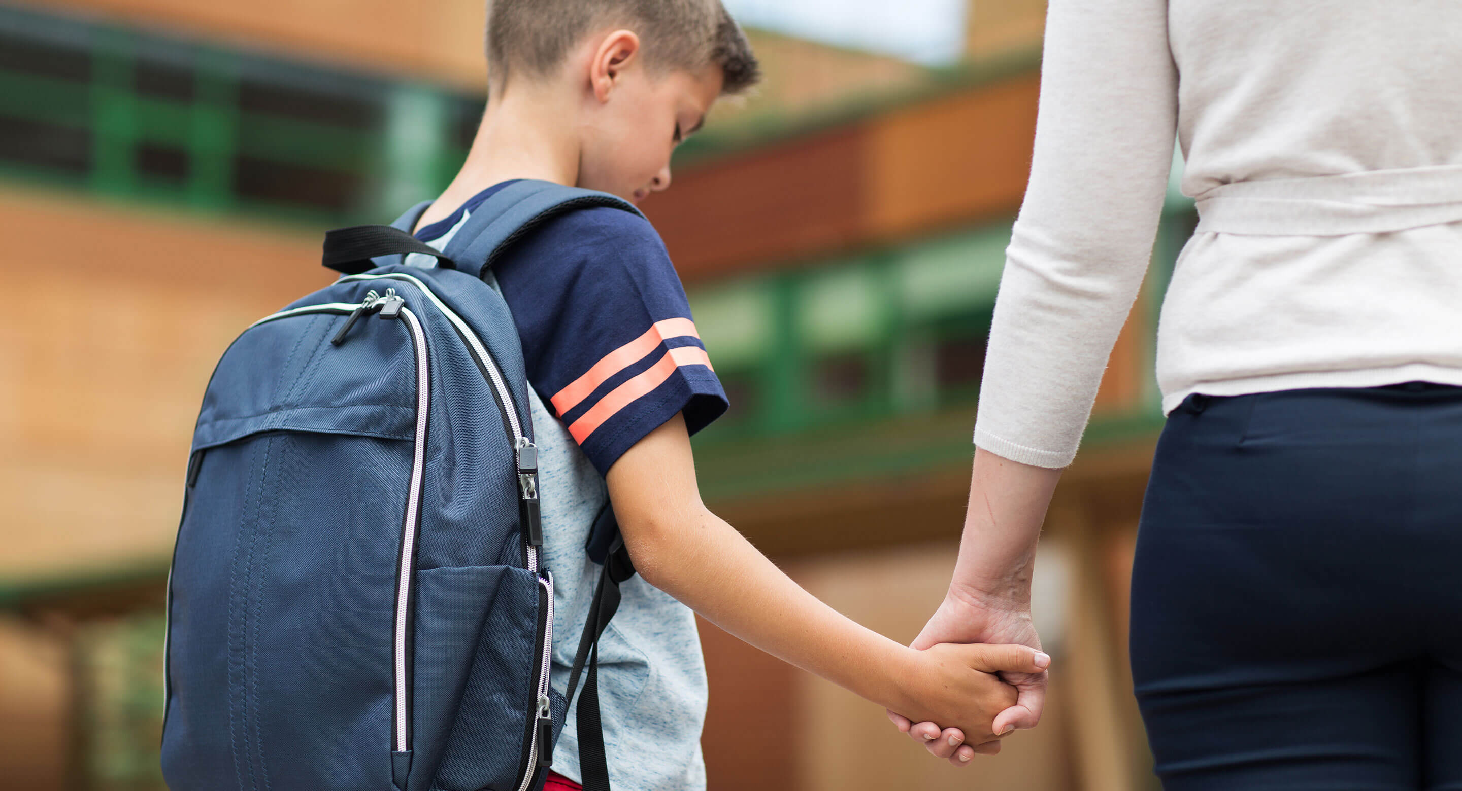 Sad boy reluctantly returning to school being lead by parent.