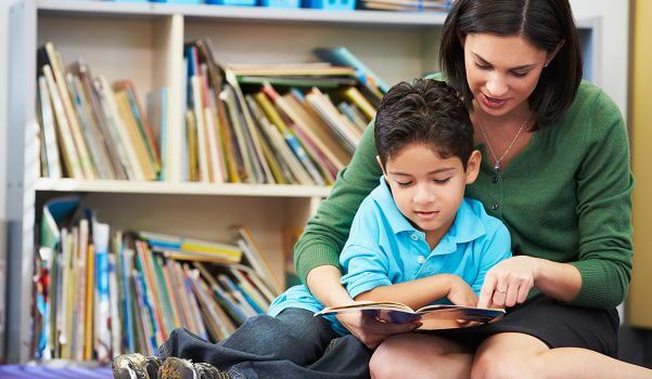 A child and a woman sitting down and reading a book together in a library. 