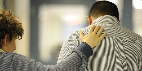 A person patting a man's back who is wearing a striped dress shirt. 