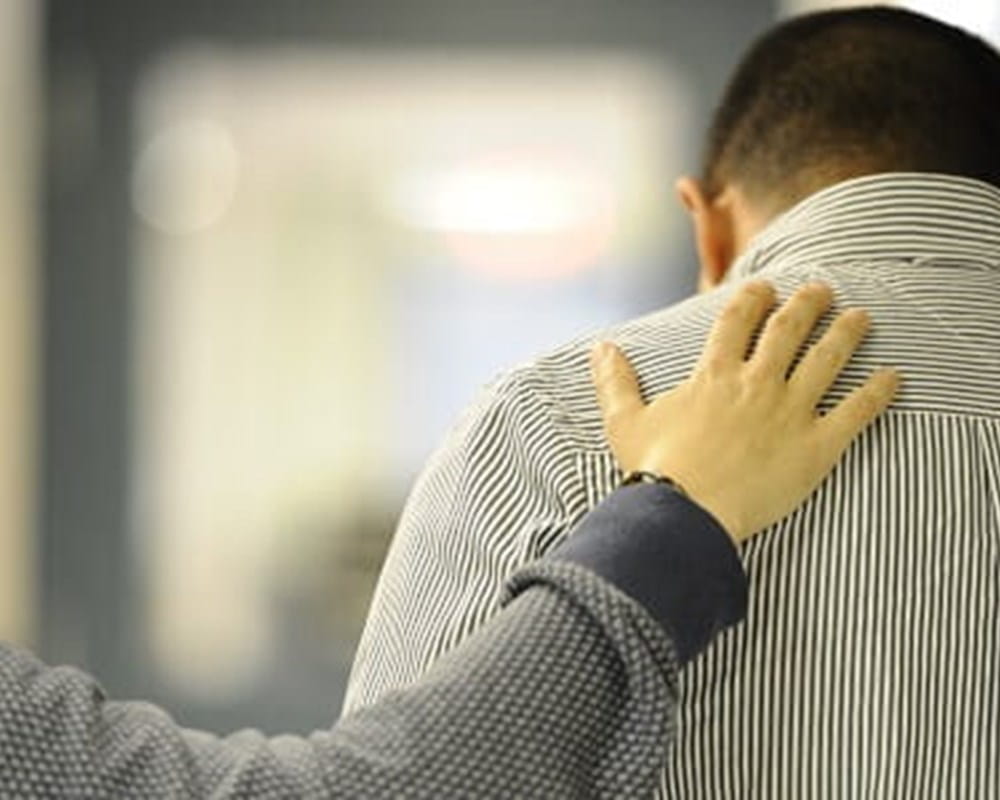 A person patting a man's back who is wearing a striped dress shirt.