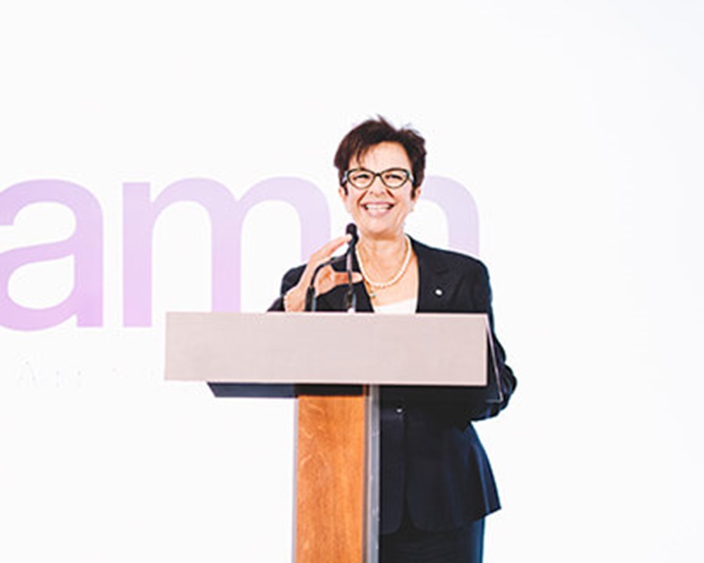 CEO, Catherina Zahn in a black blazer talking in front of a wooden podium.