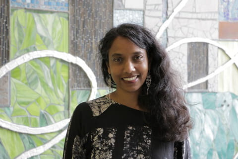A woman of colour wearing a black and white blouse smiling. 