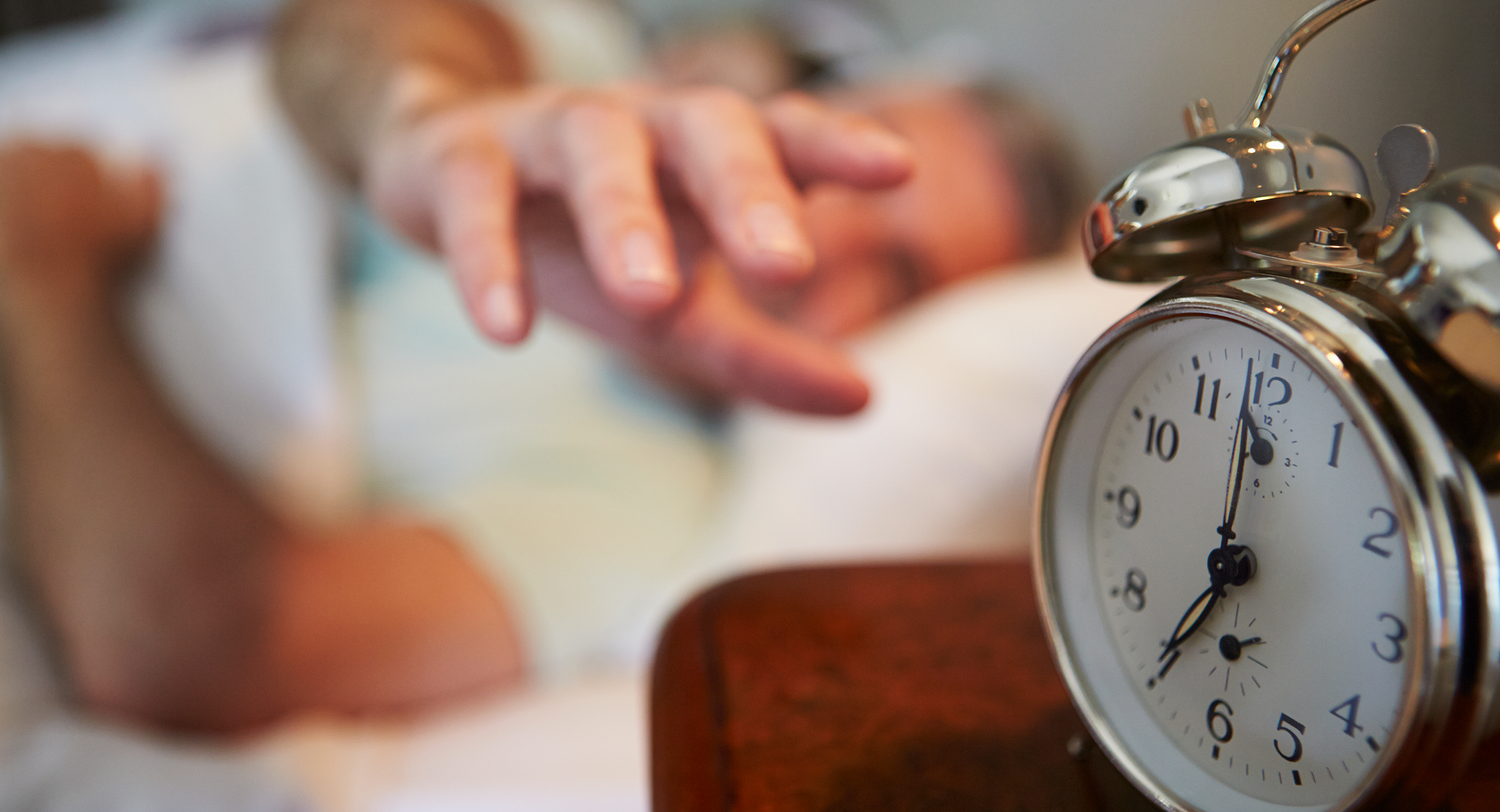 man in bed reaching for alarm clock