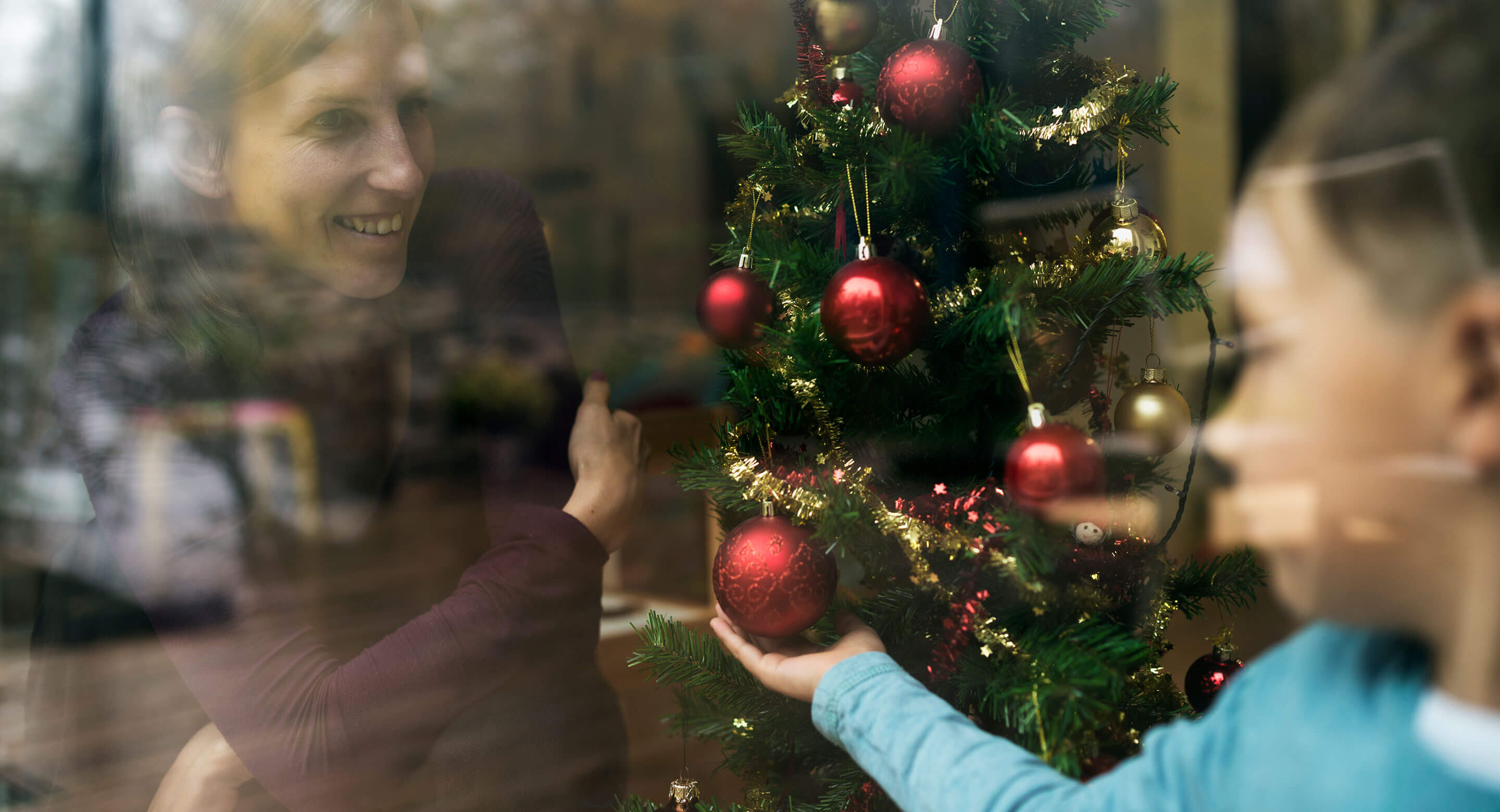 Woman watched child decorating a Christmas tree through a window.