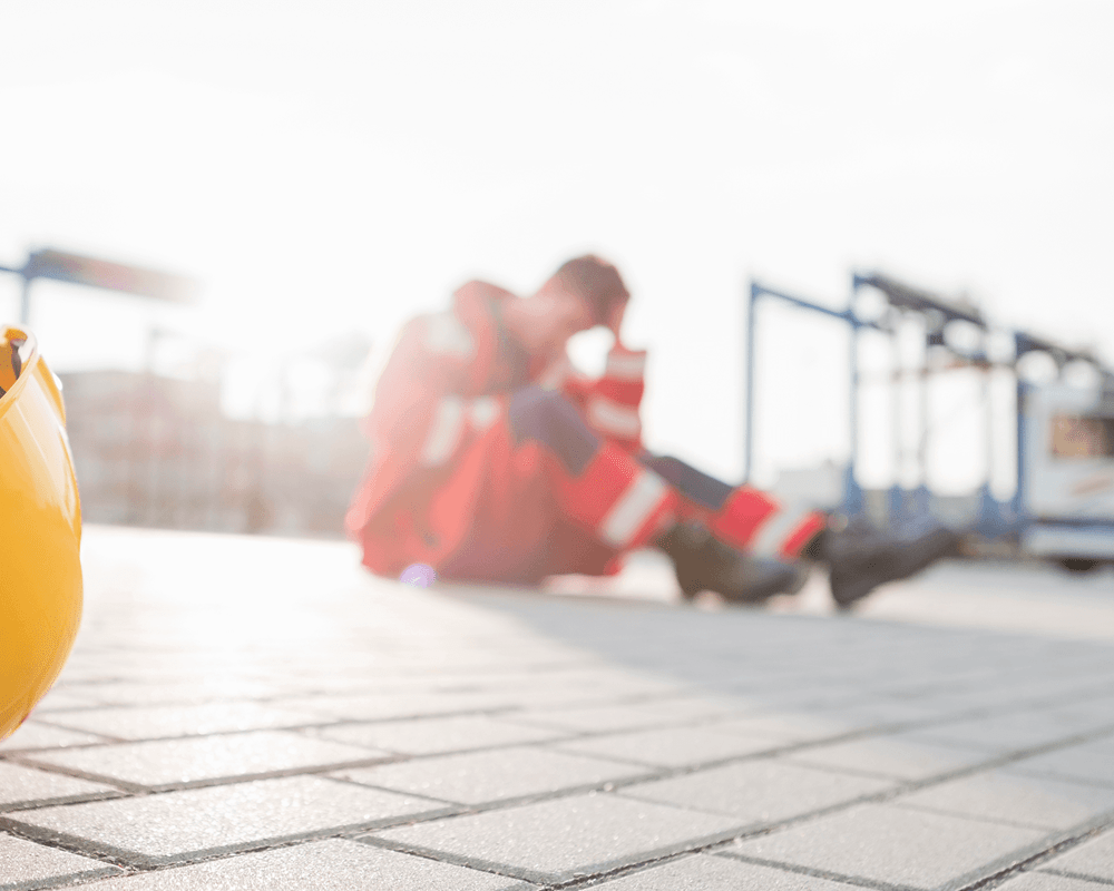 Construction worker sitting on ground, confused and worried after layoffs.
