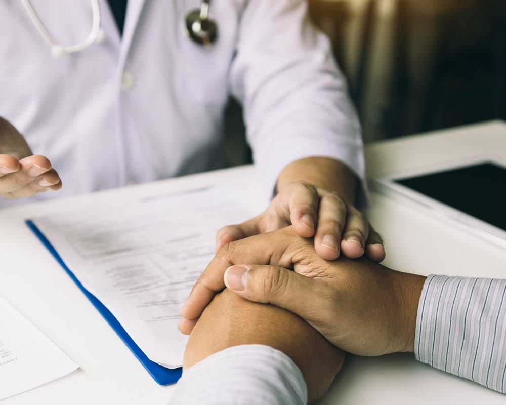 A doctor holds their hand over a patient's while explaining a situation.