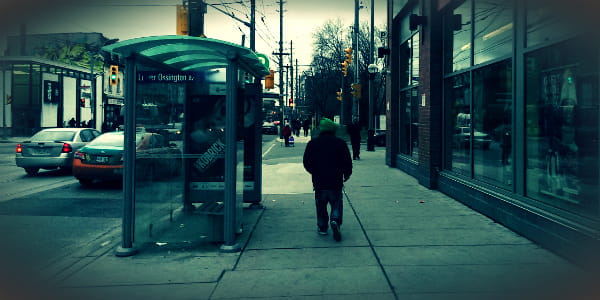 A blue tinted image of a person walking down Ossington Street. 