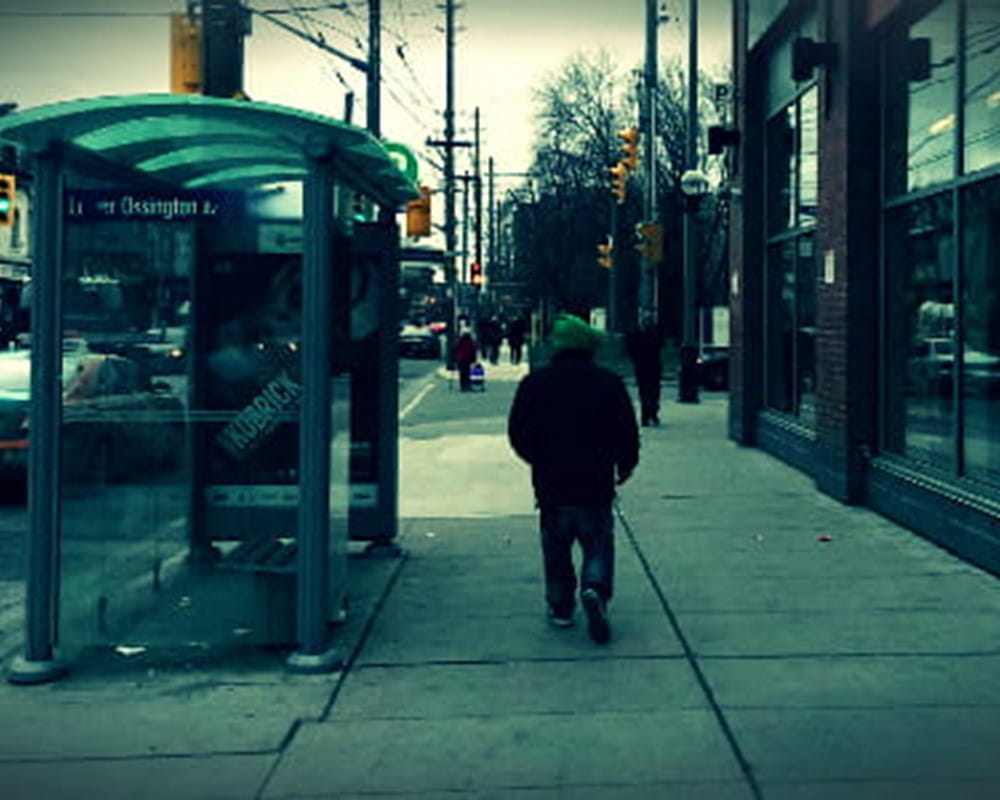 A blue tinted image of a person walking down Ossington Street.