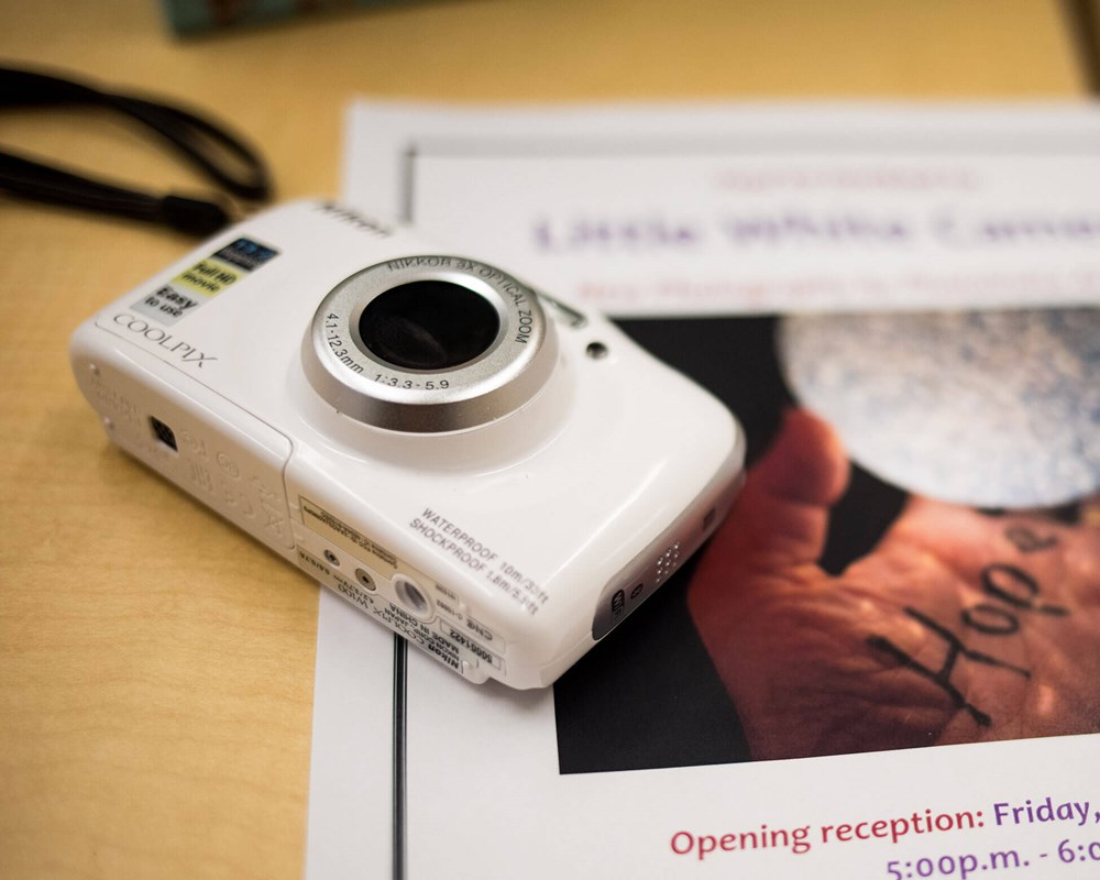 Picture of white camera beside poster for Photovoice exhibit