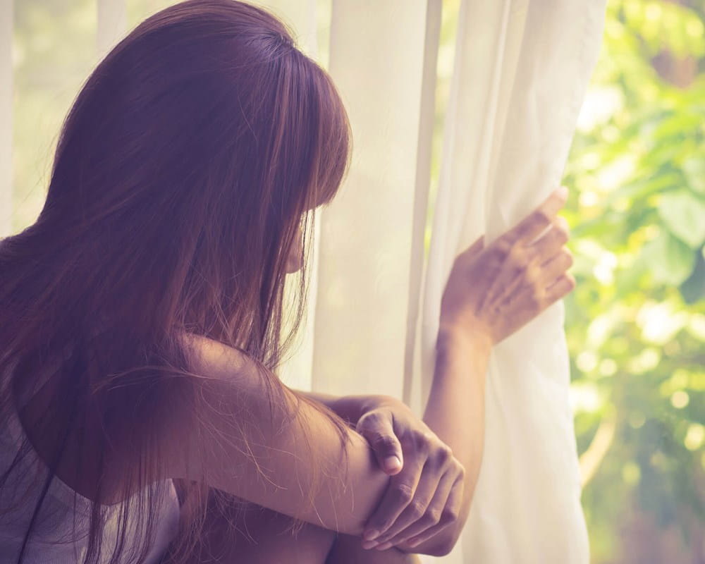 Woman standing by window looking outside