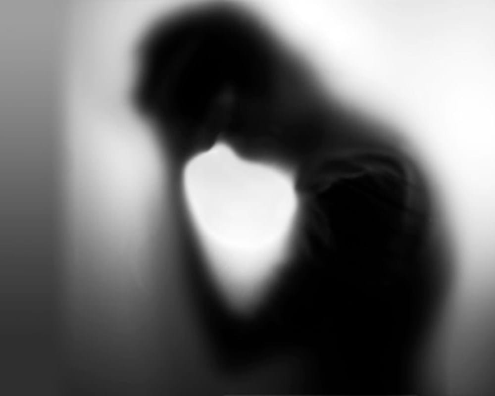 A blurry silouette of a man with his hands on his forehead.