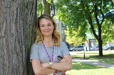 Susan Roman wearing a grey T-shirt and the purple CAMH lanyard leaning against a tree. 
