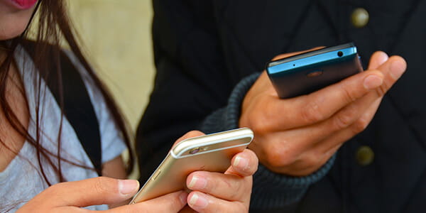 A close-up of two individuals texting one their cellphones. 