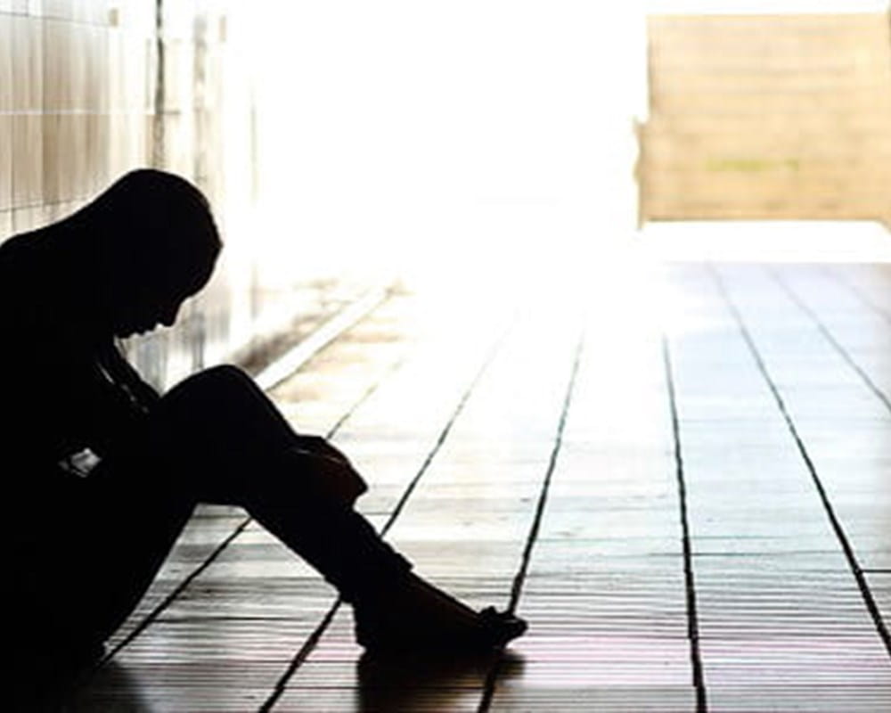 A woman sitting in a dark hallway looking down, upset.