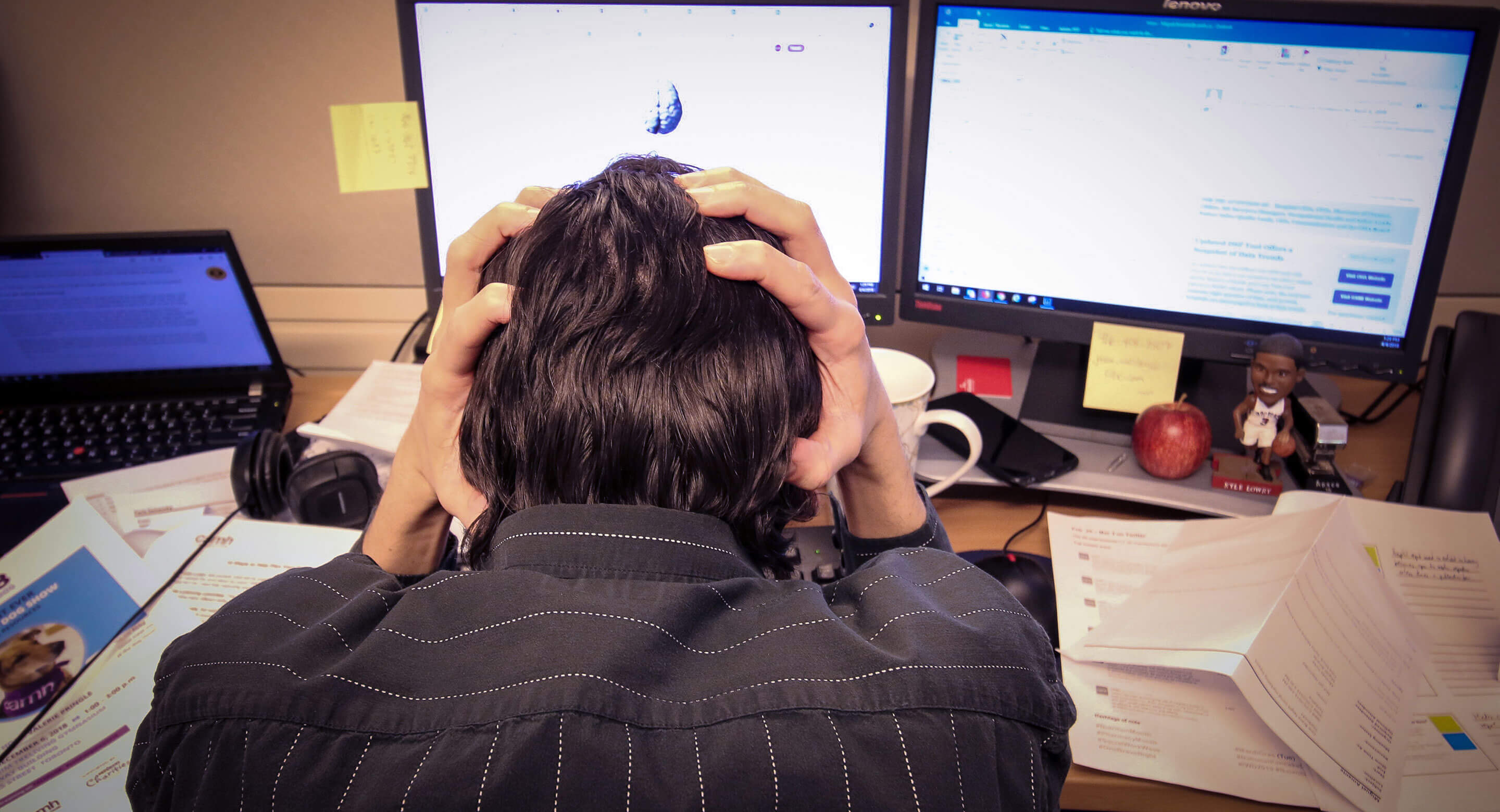 Man holding head in cluttered workspace