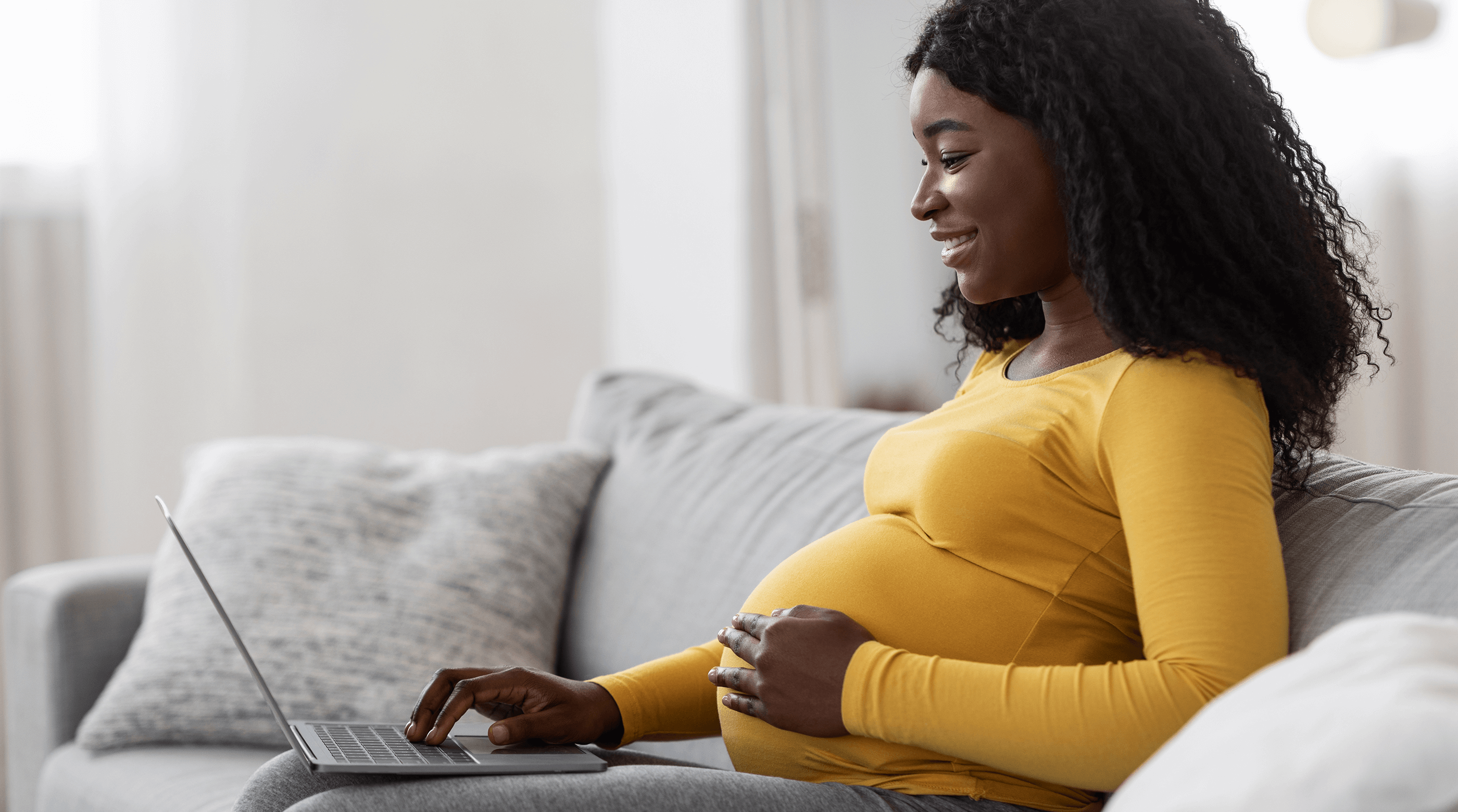 Black pregnant woman using laptop at home.