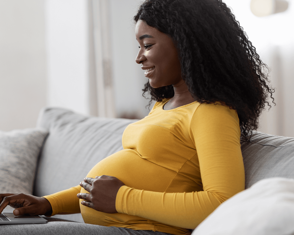 Black pregnant woman using laptop at home.